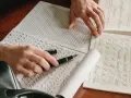 Manos practicando caligrafía con una pluma sobre hojas con ejercicios de letras.