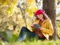 Mujer con boina roja lee un libro bajo un árbol, inspirada por los temas de cuentos del otoño.