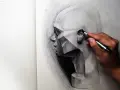 Un artista trabaja en dibujos difíciles a lápiz de un rostro geométrico, capturando la luz y la sombra con gran detalle.