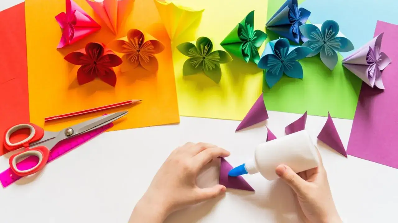 Manos creando flores de papel para manualidades del Día de la Madre. Tijeras, lápiz y pegamento listos.
