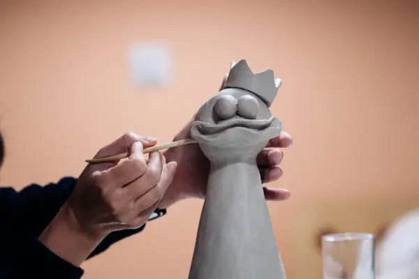 Manos trabajando con arcilla para crear una figura de rana con corona.